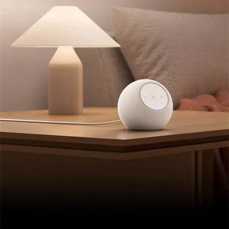 Altavoz Echo en una mesa junto a una lámpara, recortado en cuadrado para ilustrar una compra calidad precio